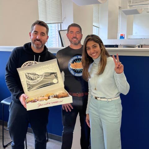 Three individuals in a dental office, one holding an open box of doughnuts with a “Dental Day” greeting, celebrating Dentist Day in Philadelphia.