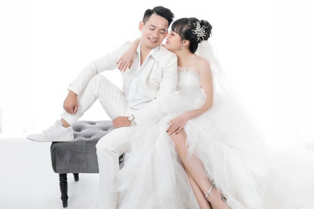 A bride and groom sitting on a bench in a white wedding dress
